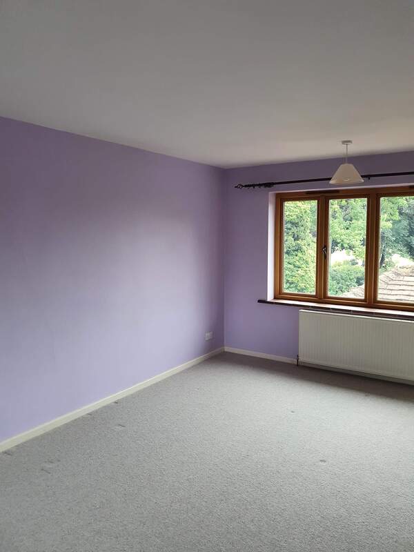 Picture of a bedroom that has been redecorated in a lilac emulsion and the skirting boards have been glossed in white. The window on the back wall of the bedroom looks to the rear garden and natural daylight is coming into the room.